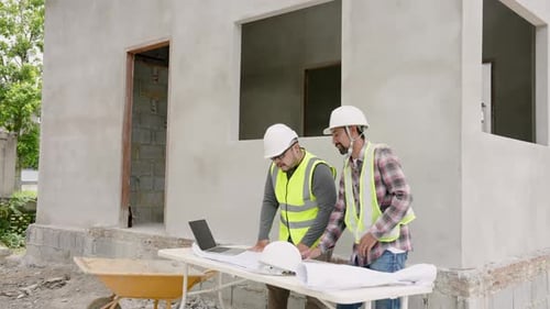 On-site house construction workers discuss building plan. Asian engineers in white helmets and yello