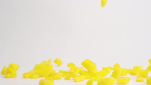 Gewürfelte gelbe Paprikastücke, die auf eine weiße Tischplatte fallen und in Zeitlupe zu einem Stapel hüpfen
