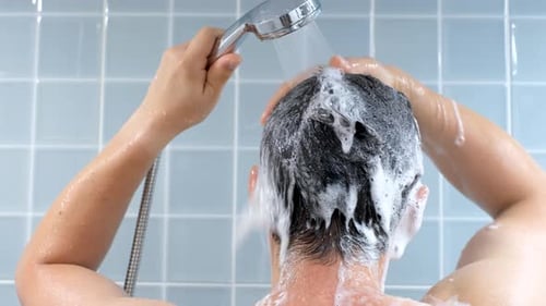 Man washing his hair in the shower against background of blue tiles, rear view.