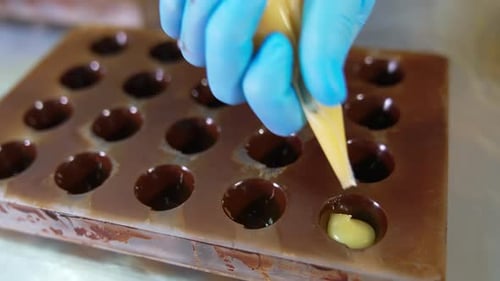 Gloved hand squeezes white filling from pastry bag into molds. Close up.