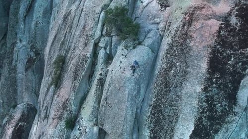 Ascending aerial drone shot focused on a tiny climber while ascends by a granite rock wall