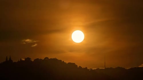 Time lapse of the sun setting over hills that are covered with clouds.