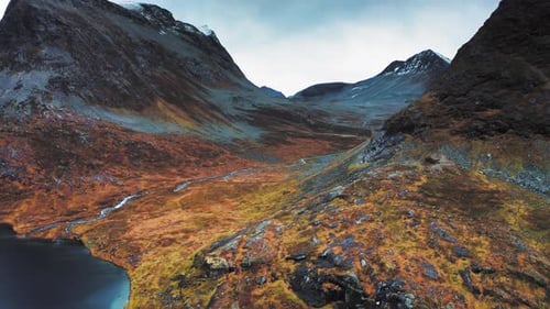 Aerial view of a serene valley in autumn, with a stream winding through the vibrant landscape toward