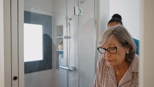 Senior woman walks with caregiver support in bathroom