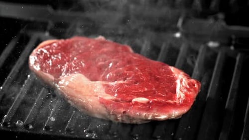 Raw Marbled Steak Grilling on Black Grill