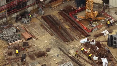 Aerial orbital shot around a crane hook chain with construction workers organizing rebar and formwor