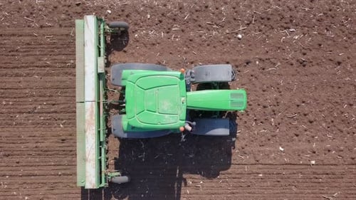 Green Tractor cultivating and seeding a dry field - Top down aerial footage