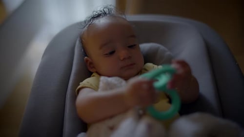 Cute Baby Sitting in a Cozy Chair Holding a Green Teething Toy Radiating Innocence and Joy