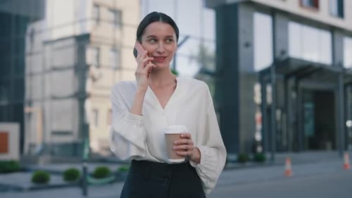 Attractive Confident Caucasian Businesswoman Walking on Street in City and Speaking on Mobile Phone