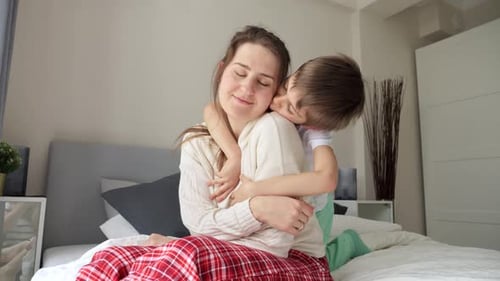Child Hugging Smiling Mother in Bedroom