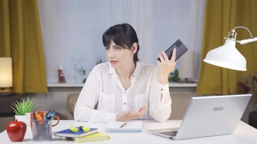 Woman Talking on Smartphone at Desk with Laptop