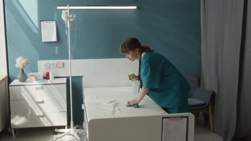 Nurse Wiping Mattress with Cloth Carrying out Wet Cleaning in Hospital Room