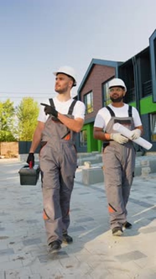 Dos constructores caminando cerca de una moderna construcción de casas adosadas
