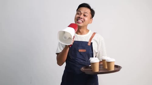 A male coffee shop waiter wearing an apron shouts out to customers using a megaphone while carrying