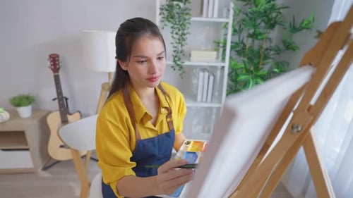 Asian young talented woman artist coloring on painting board in house.