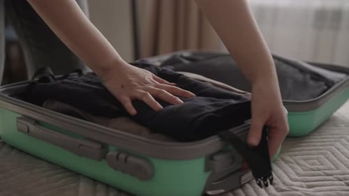 Woman Packing Suitcase with Clothes on Bed