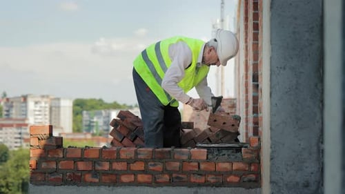 Mason Working on Brick Wall at Construction Site A Construction Worker in a Highvisibility Vest is