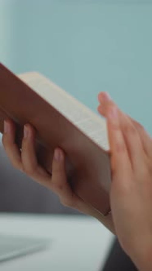 Female Student Holds Book Flipping Pages to Find Information