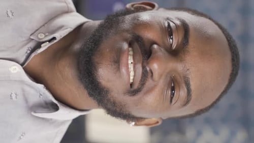 Vertical Video of African employee looking at camera and laughing. He's in his office.