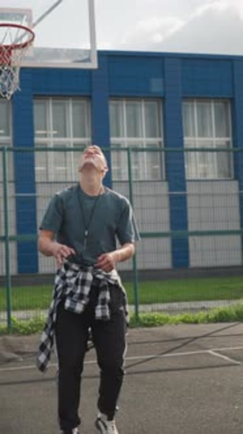 Sport Man Throws Up Volleyball Jumps and Hits It on Basketball Court with Blue Building Background