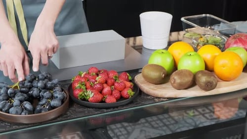 The pastry chef shows fruits and berries. The girl prepares a fruit salad with strawberries and grap