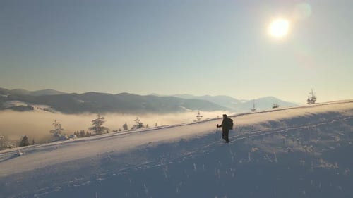 Hiker with Backpack Walking on Snowy Mountain Hillside on Cold Winter Day