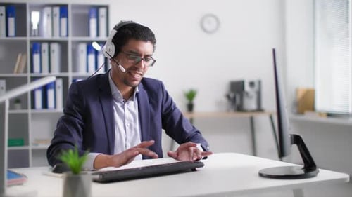 African American Male Office Worker Working at Computer and Chatting with Client Using Headset to