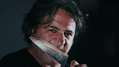 Adult Holding Knife Between Teeth in Dark Setting