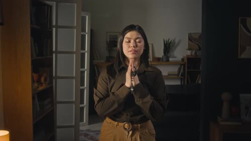 Woman Praying with Rosary Beads in Dark Home
