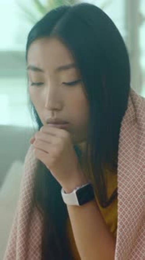 Asian Woman Lying Under Blanket Quiet Scene of Asian Woman Resting with Smartwatch and Soothing