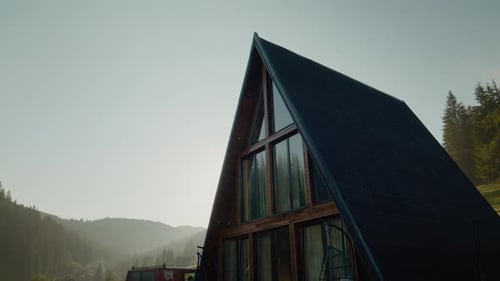 Morning sunlight illuminates A-frame cabin nestled in serene mountain landscape