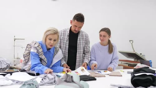 Group of Three Diverse Fashion Dressmakers Looking at Fabric Samples and Discussing Ideas for