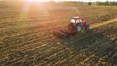 Tractor Plowing Field in Cultivated Land and Soil Tillage Aerial View with Beautiful Sunset Beams