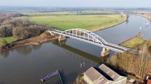 Aerial view of arched highway bridge over curving river, linking green fields, trees, and scattered
