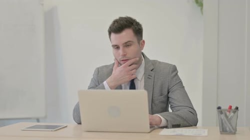 Young Businessman Thinking while Working on Laptop