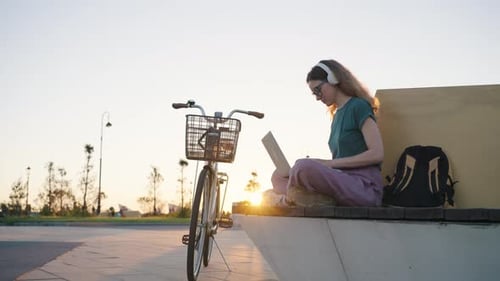 Junge Studentin tippt in einem Laptop, Freelancerin, sitzt auf einer Bank in einem Stadtpark und arbeitet an einem