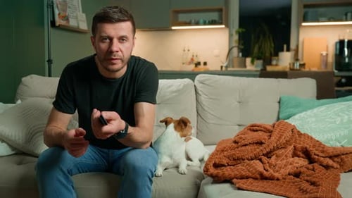 Man with Dog Sits on Couch with Remote