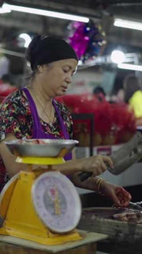 Senhora asiática madura cortando peixe cru em pedaços antes de pesá-lo em grande escala em um mercado local