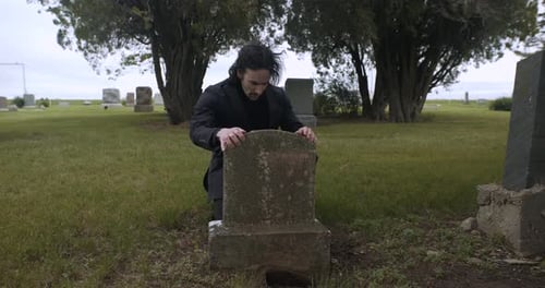 Sad, emotional man in grief over death of loved one in cemetery.