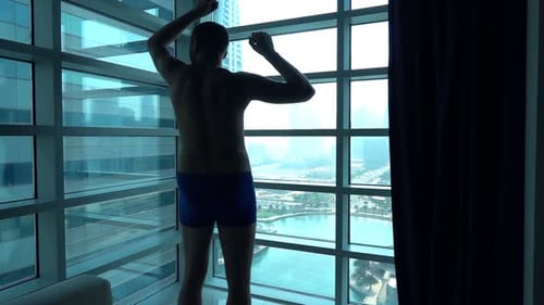 Man Stretching in Apartment Overlooking City Skyline