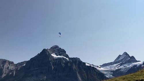 Gleitschirm fliegt über verschneite Berge bei blauem Himmel