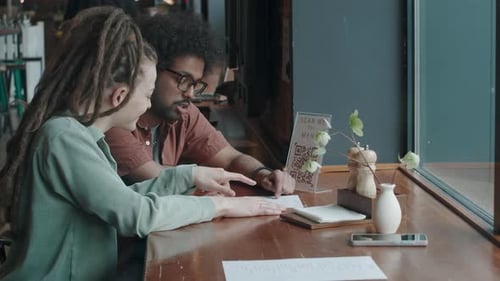 Man and Woman Sitting in Restaurant, Talking and Smiling, while Examining Menu