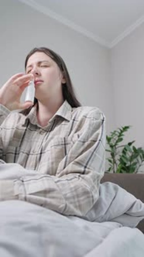 Femme malade enveloppée dans une couverture allongée sur le canapé à la maison, utilisant des gouttes nasales, traitant les conges nasales