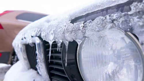 Close-up of a snow-covered car grille with icicles forming on headlights