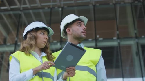 Man and Woman Engineers Have Conversation and using Tablet Computer on Construction Site. Glass Bui