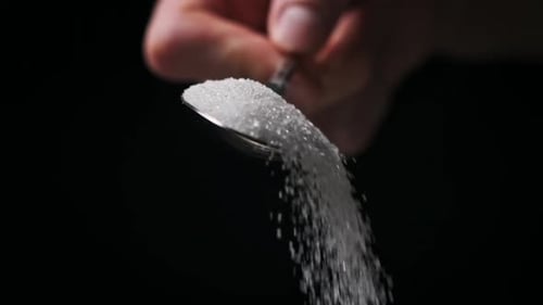 Sugar Falling From a Full Spoon on Black Background in Slow Motion CloseUp