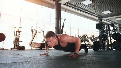 Young sportive strong man in black wear doing push-ups in gym