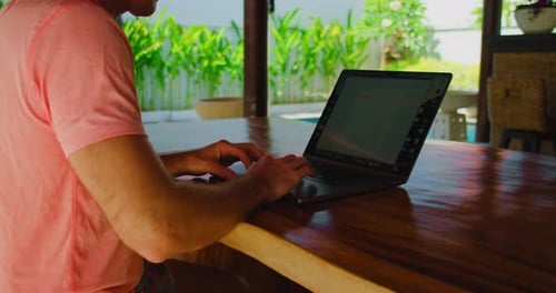 Gros plan de mains d'homme tapant sur un ordinateur portable dans le jardin sur une table en bois. Homme travaillant sur un clavier d'ordinateur