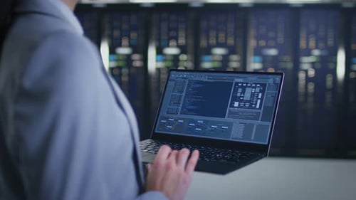 Close Up Shot of an IT Specialist Working on Laptop in Data Center Next to Server Racks. Computer i
