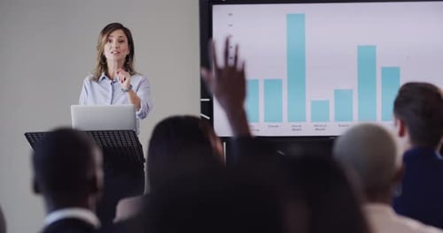 Audience of business people asking the speaker a question while lifting their hands during